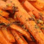 Close-up of roasted baby carrots garnished with chopped herbs and small bits of garlic.
