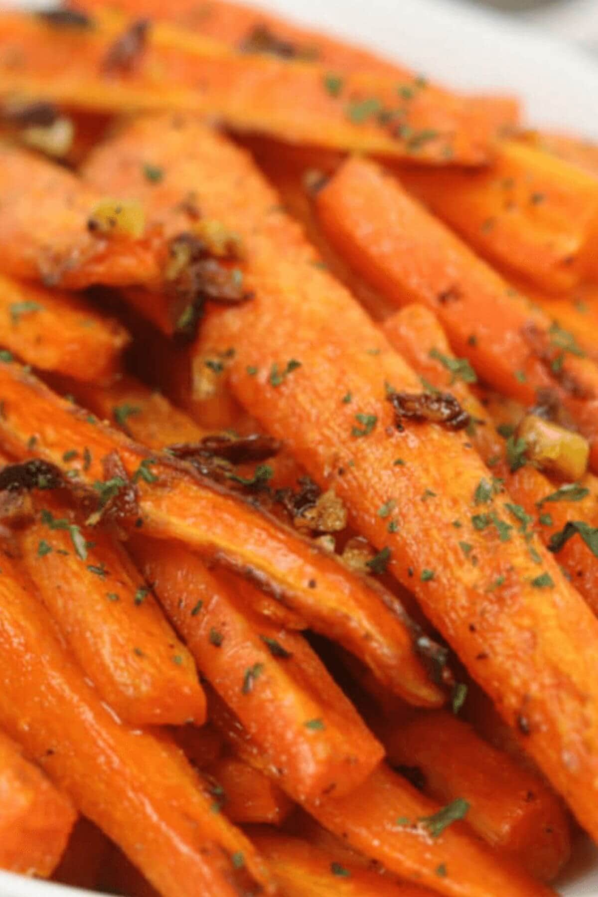 Close-up of Roasted Baby Carrots cut into sticks, garnished with chopped herbs and bits of seasoning.