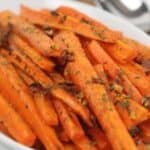 A white dish filled with roasted baby carrots cut into sticks, garnished with chopped herbs and small pieces of garlic.