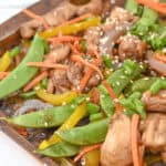A tray of meal features stir-fried snow peas, bell peppers, and carrots, all topped with sesame seeds and chopped green onions.