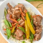 A bowl of rice topped with honey sesame chicken, snow peas, yellow bell peppers, carrots, and onions delivers a delightful crunch and sweet savory flavor.