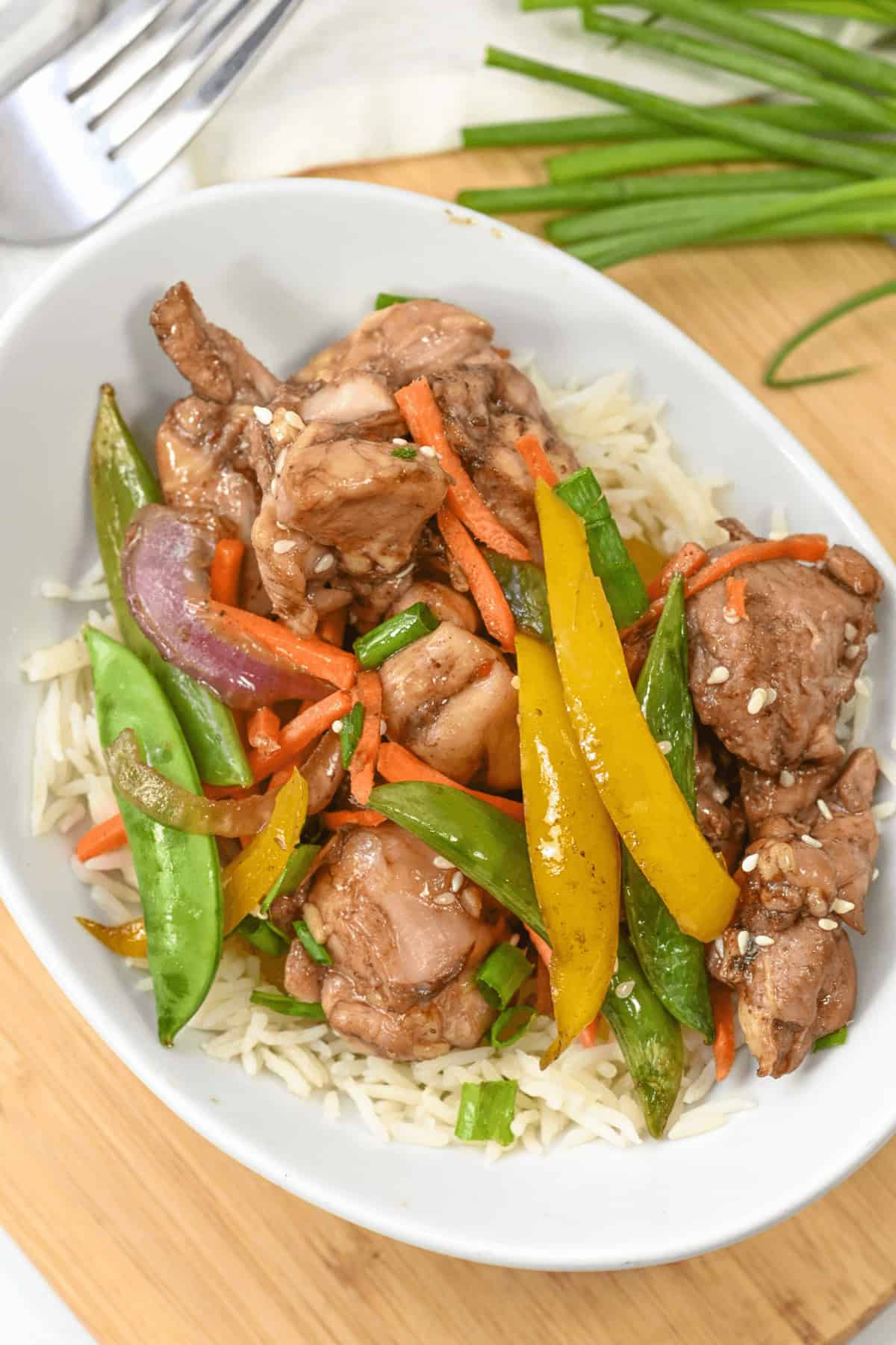 A bowl of rice topped with honey sesame chicken, snow peas, yellow bell peppers, carrots, and onions delivers a delightful crunch and sweet savory flavor.