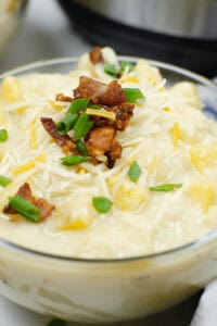 A bowl of creamy Instant Pot Loaded Potato Soup topped with crumbled bacon, shredded cheese, and chopped green onions.