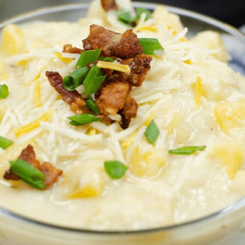 A bowl of creamy Instant Pot Loaded Potato Soup topped with crumbled bacon, shredded cheese, and chopped green onions.