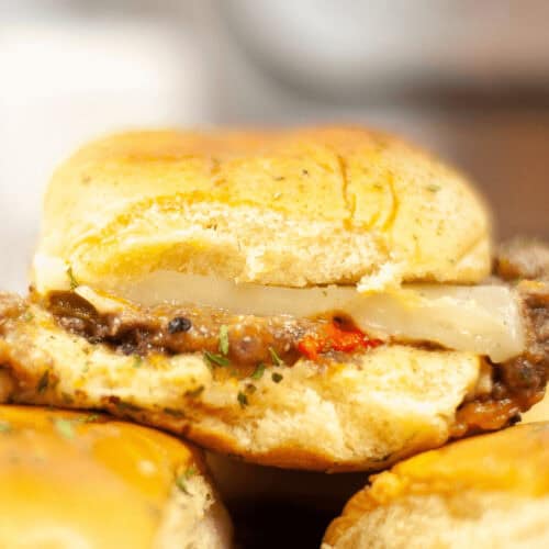 Close-up of a steak slider cheeseburger with a slice of onion, served on a bun.