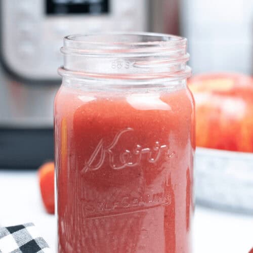 A jar of delicious instant pot strawberry applesauce with an instant pot in the back.