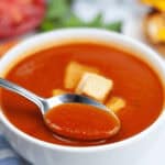 A bowl of the dish with a spoon in it and croutons on top.