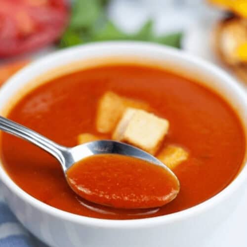 A bowl of the dish with a spoon in it and croutons on top.