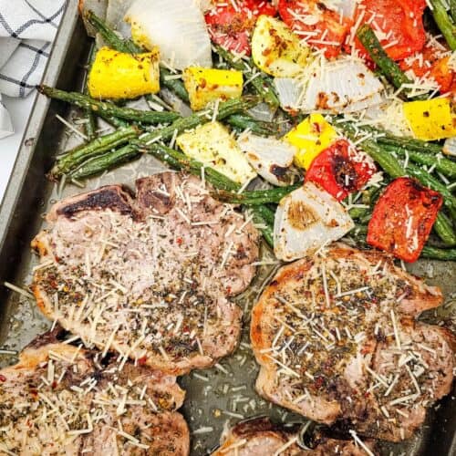 Meat alongside roasted green beans, tomatoes, onions, and yellow squash, all sprinkled with grated cheese for a delicious one-pan meal.