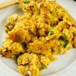 A serving of Jiffy Cornbread Dressing with visible pieces of celery and onion sits on a white plate, accompanied by a wooden fork.