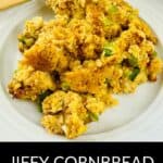 A serving of Jiffy Cornbread Dressing with visible green vegetables sits on a white plate, accompanied by a wooden fork; text reads "Jiffy Cornbread Dressing.