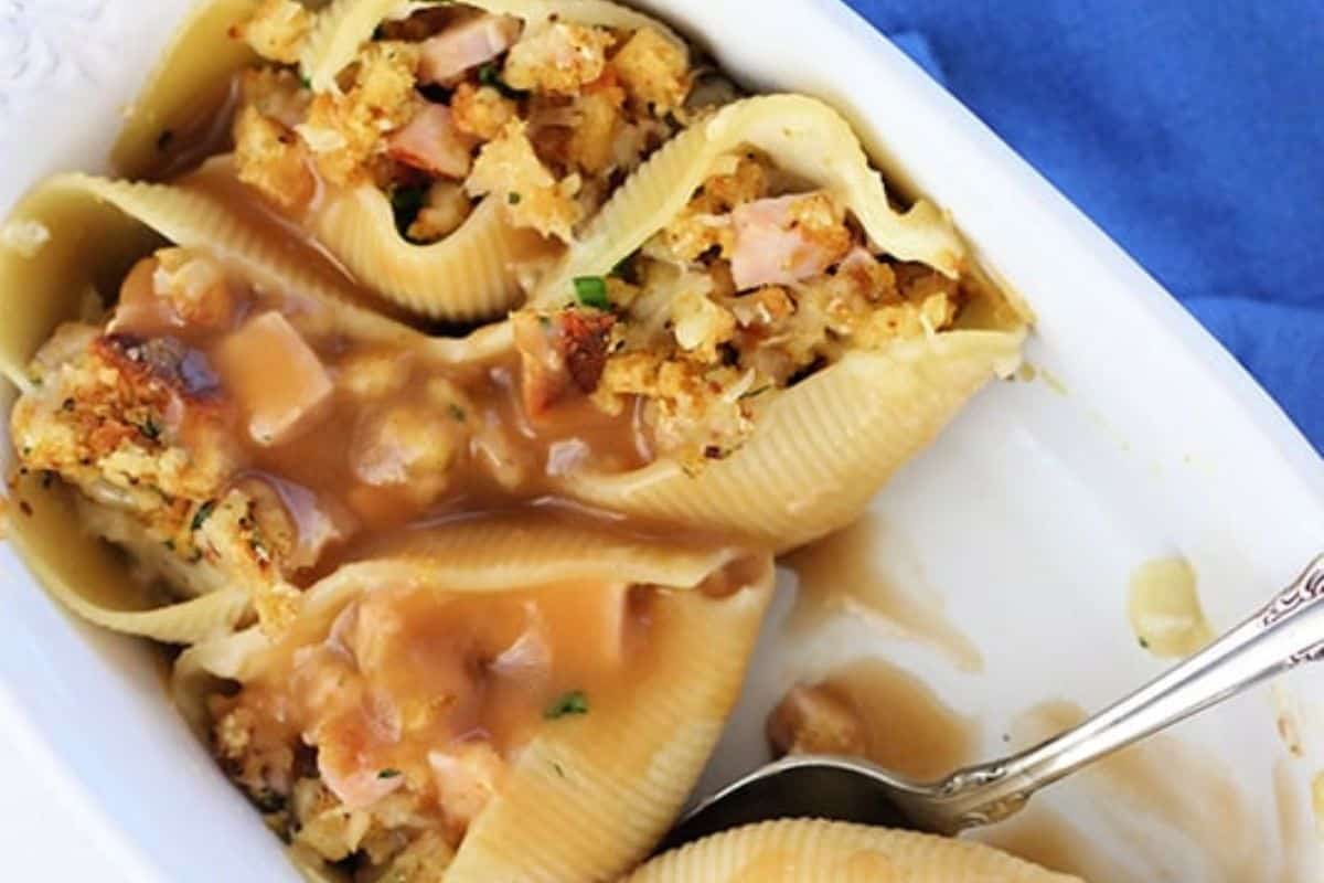 A white serving dish of Thanksgiving leftover stuffed shells, filled with turkey, stuffing, and gravy. 
