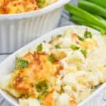 Savor the deliciousness of a Cheesy Cauliflower Casserole, topped with green onions and crispy bits. Served on a white plate, this dish is complemented by a white baking dish and fresh green onions in the background.
