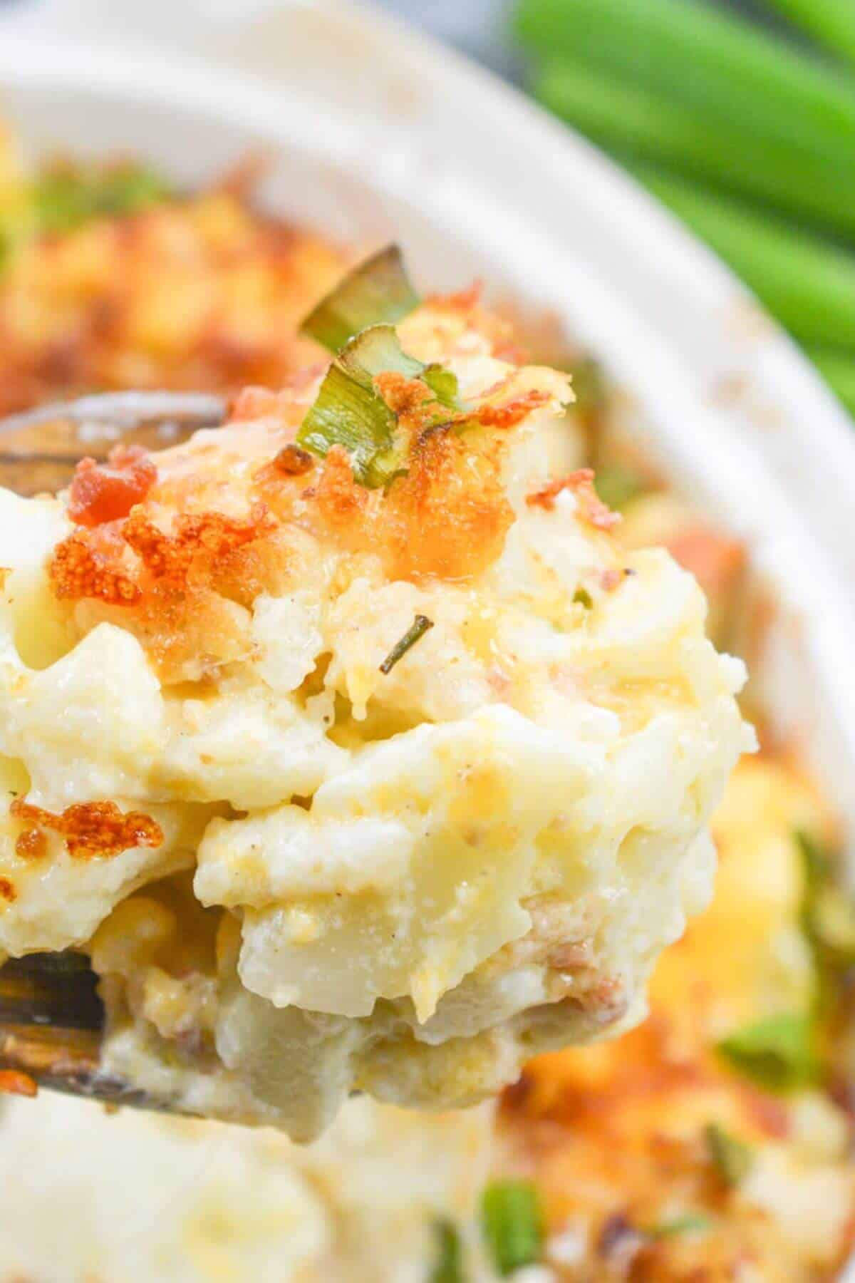 A close-up of a cheesy cauliflower casserole with a golden-brown crust and green onions on top, held invitingly in a serving spoon.