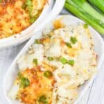 A delightful dish of cheesy cauliflower casserole topped with melted cheese and green onions, nestled beside a bunch of fresh green onions on a rustic wooden surface.