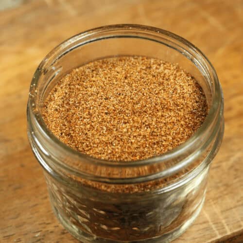 A glass jar filled with low sodium taco seasoning on a wooden surface.