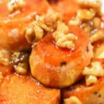 Close-up of the dish, sliced, roasted sweet vegetables topped with glazed walnuts on a white plate.