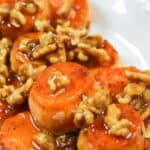 Sliced Maple Sweet Potatoes glazed and topped with walnuts and syrup are served on a white plate.