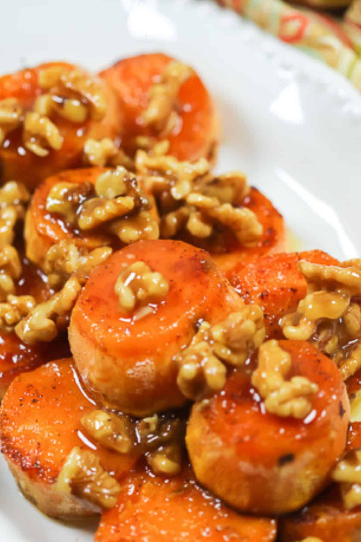 Sliced Maple Sweet Potatoes glazed and topped with walnuts and syrup are served on a white plate.
