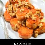 Maple Sweet Potatoes are sliced and topped with walnuts and maple glaze, served on a white plate with a silver spoon.