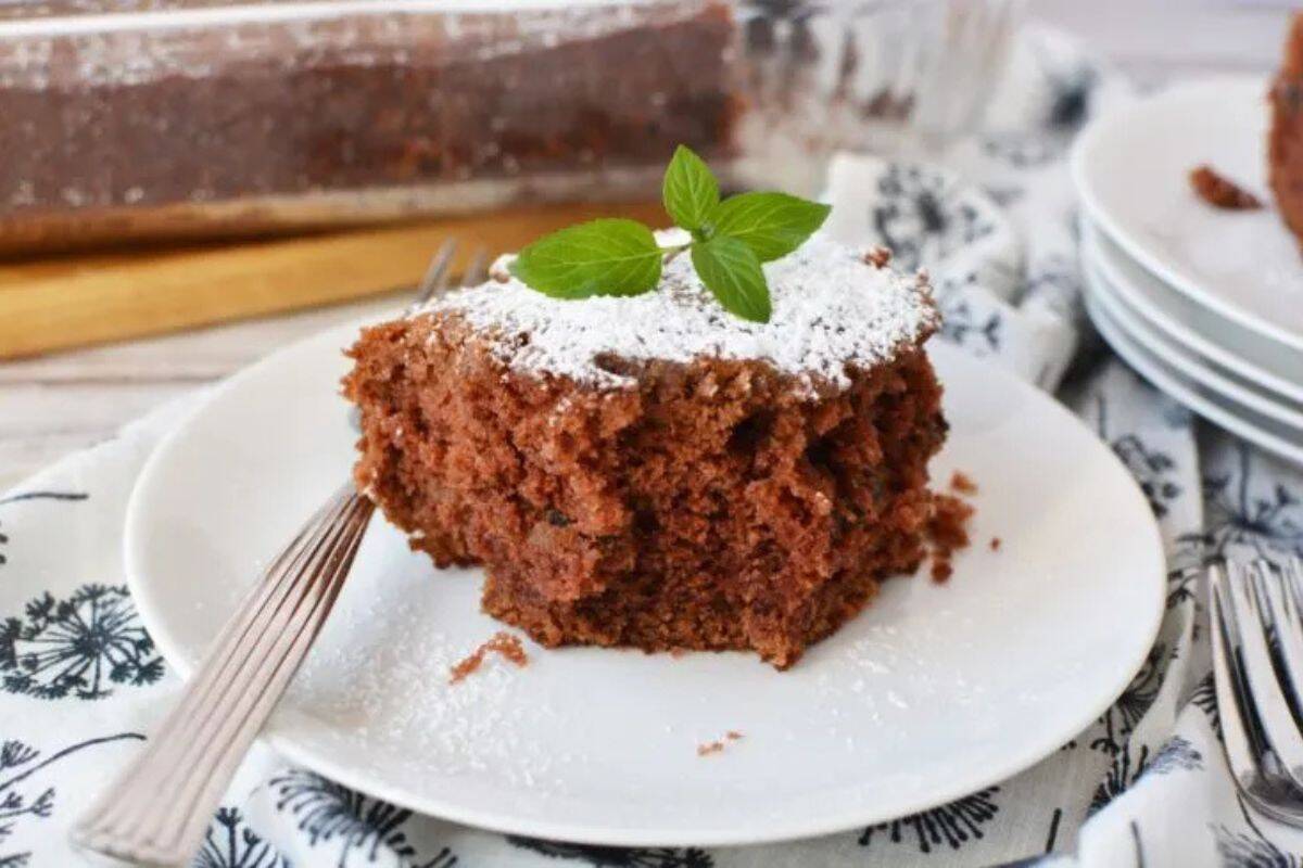 A close-up of a piece of mashed potato chocolate cake served on a white plate with powdered sugar on top.