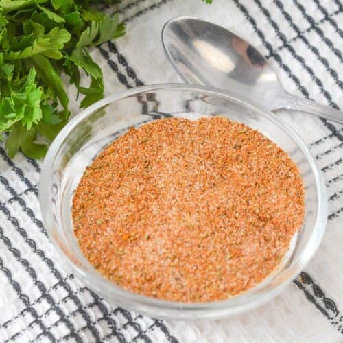 A bowl of meatloaf seasoning rests on a striped kitchen towel, surrounded by fresh parsley and a spoon.