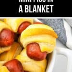 A white dish holds Mini Pigs in a Blanket made from crescent rolls and sausages, with a gray and white cloth in the background.