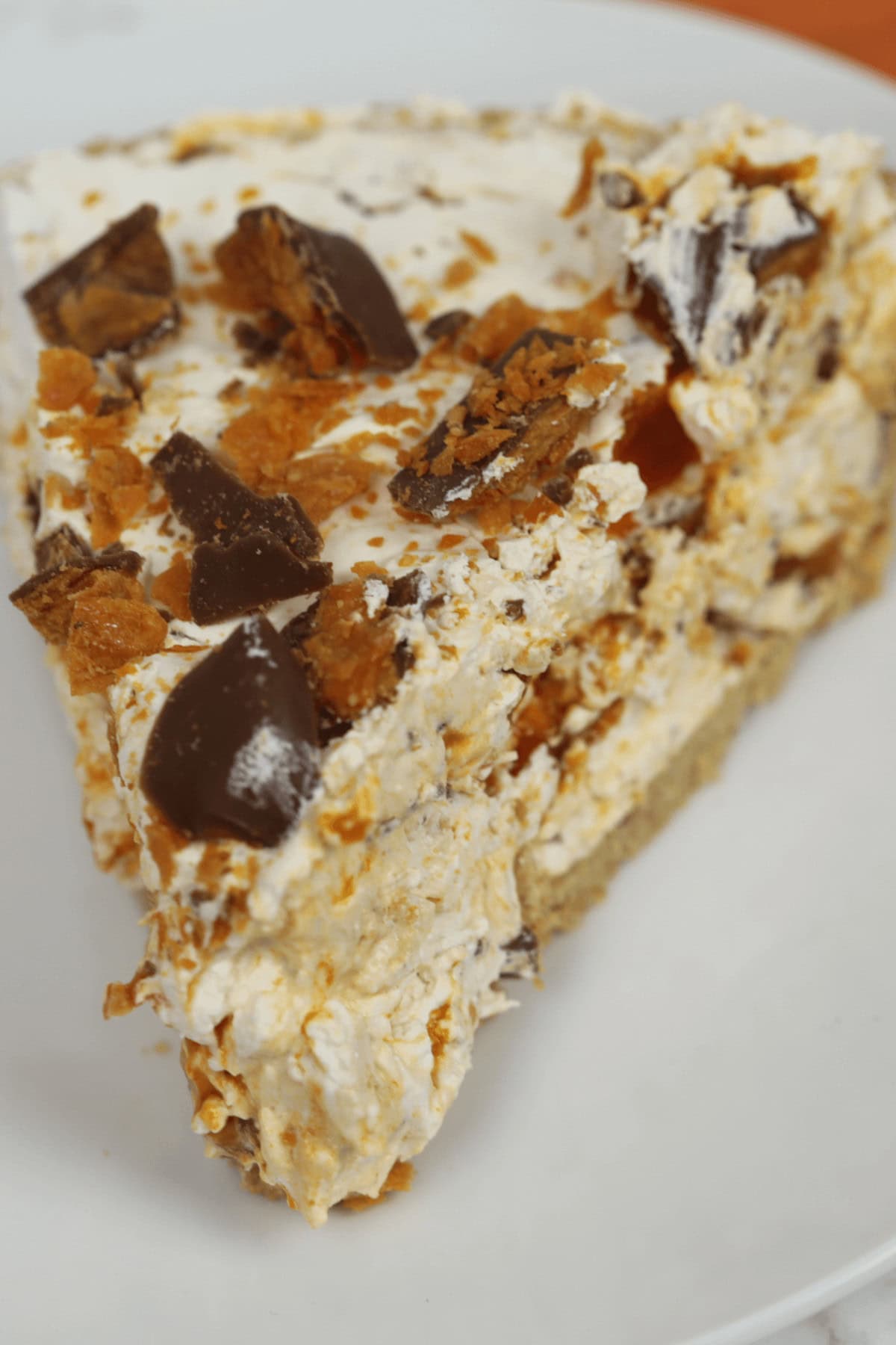 A slice of Butterfinger Pie with crumbled chocolate pieces and a creamy filling sits enticingly on a white plate.