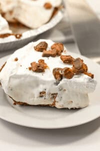 A slice of creamy caramel pie topped with crumbled chocolate pieces on a white plate.