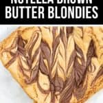 A pan of Brown Butter Blondies with a marbled Nutella swirl pattern on top sits on a white surface, showcasing the rich, golden layers and irresistible chocolatey finish.