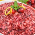 A bowl of the Recipe topped with whole fruit, a lemon twist, and a mint sprig, with a sliced lemon in the background.