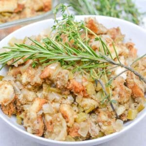 A bowl of Old Fashioned Stuffing with chopped celery and onions, garnished with fresh rosemary and thyme sprigs.