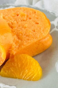 Close-up of a sliced Orange Jello Salad mold on a plate, with a mandarin orange slice elegantly garnishing the side.