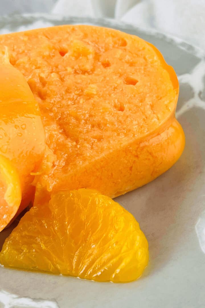 Close-up of a sliced Orange Jello Salad mold on a plate, with a mandarin orange slice elegantly garnishing the side.