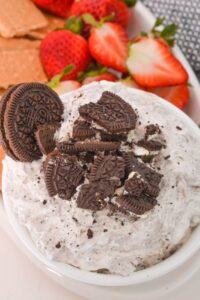 A bowl of luscious Oreo Dip, crowned with crushed chocolate sandwich cookies, sits invitingly among juicy strawberries and crisp graham crackers.