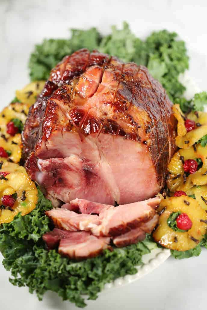 Pineapple Glazed Ham shot from the top on a white dish surrounded by pineapple and greens