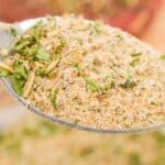 A close-up of a spoon holding a blend of dried herbs and spices, including green leafy pieces and coarse powder—perfect for your homemade Pot Roast Seasoning recipe.