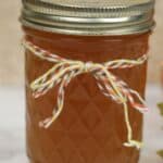 A glass jar filled with amber-colored Pumpkin Pie Moonshine, sealed with a metal lid and decorated with a red, yellow, and white twine bow.