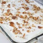 A glass baking dish filled with dessert topped with creamy white frosting and a generous layer of chopped pecans.