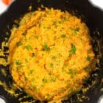 A black pot filled and topped with garnish with chopped parsley and shown on a white background.