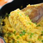 A wooden spoon holding a serving of garnished with chopped parsley over a pot filled with more of the same dish.