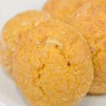 Three golden brown dessert with a sugar coating are arranged on a white plate.