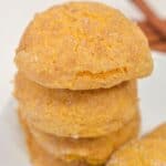 A stack of four round, golden-brown Pumpkin Snickerdoodle Cookies with a sugar-dusted, cracked surface sits on a white plate.