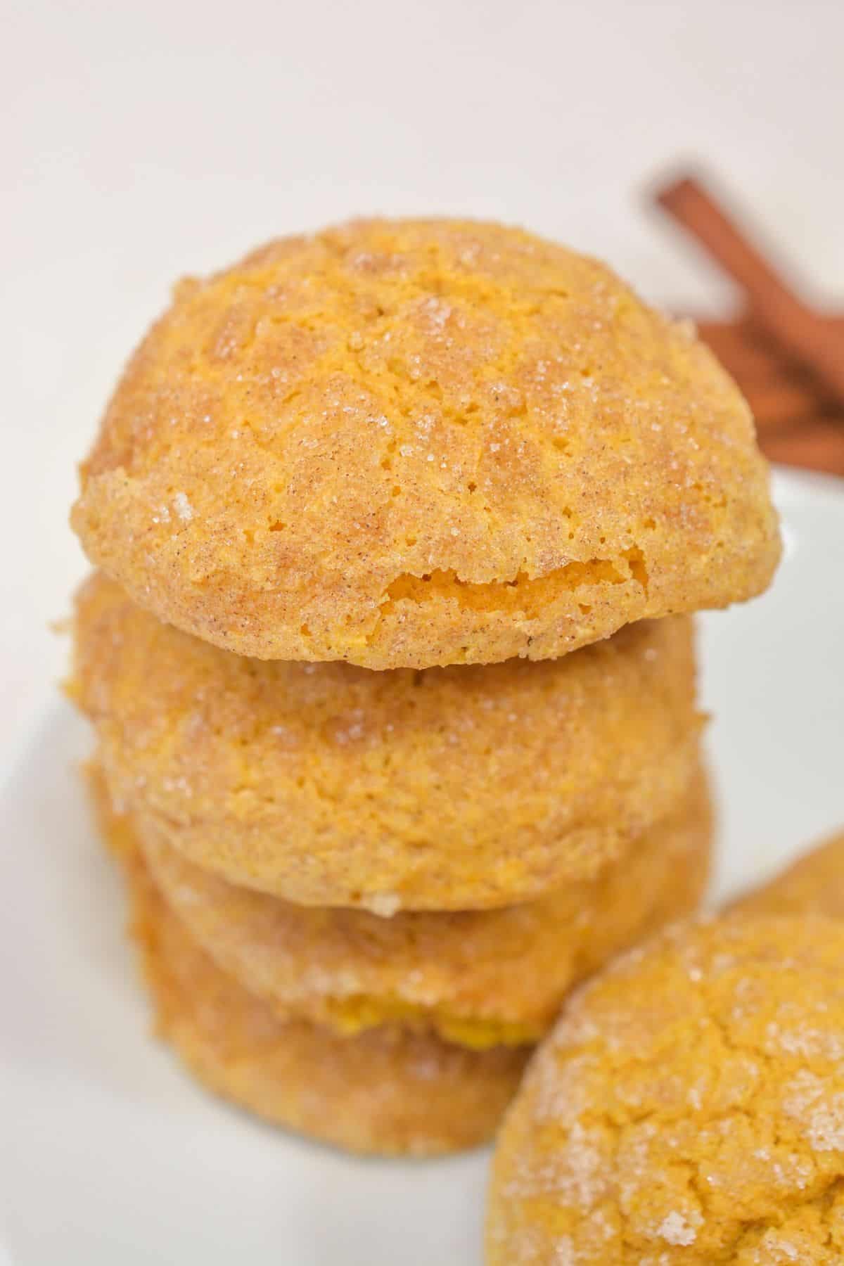 A stack of four round, golden-brown Pumpkin Snickerdoodle Cookies with a sugar-dusted, cracked surface sits on a white plate.