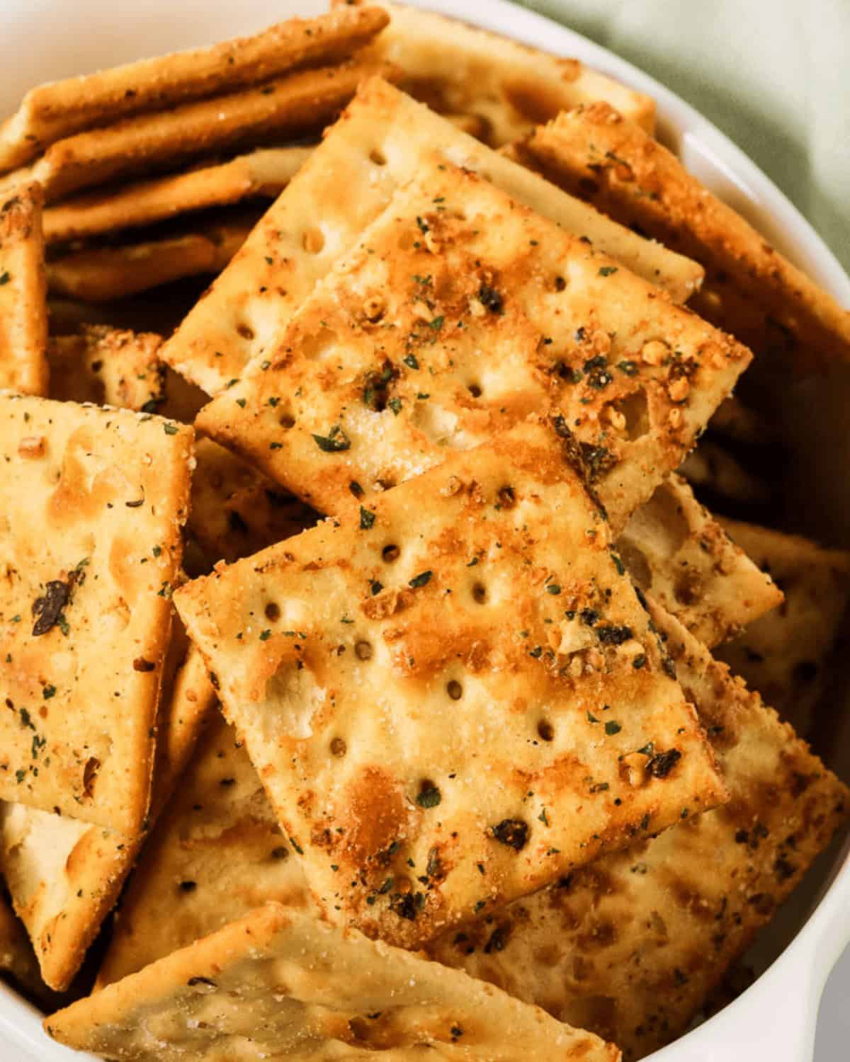 A close-up view of a bowl filled with seasoned ranch spicy crackers topped with herbs.