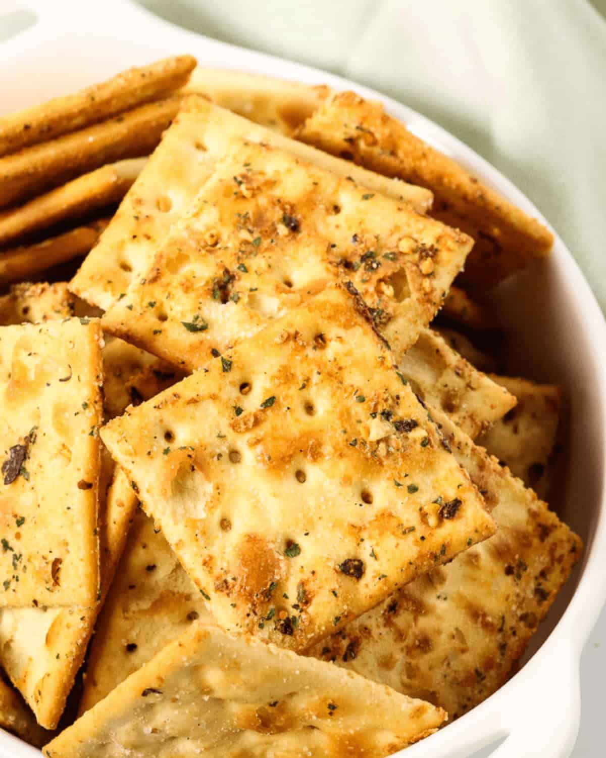 A bowl filled with seasoned ranch spicy crackers, featuring a golden-brown color and sprinkled with herbs and spices.