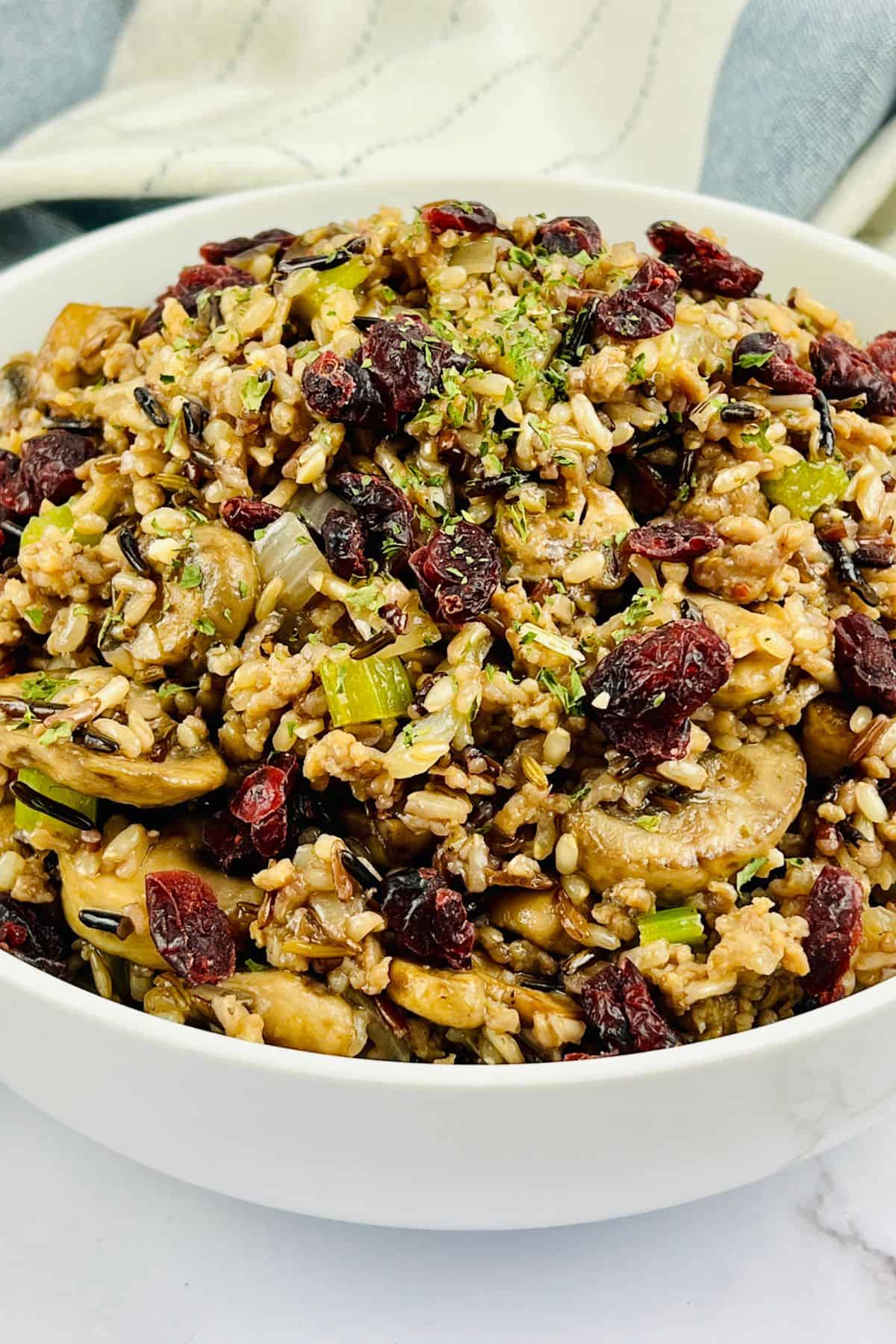 A bowl filled with a mixed wild rice dressing featuring mushrooms, celery, and dried cranberries, garnished with fresh herbs.