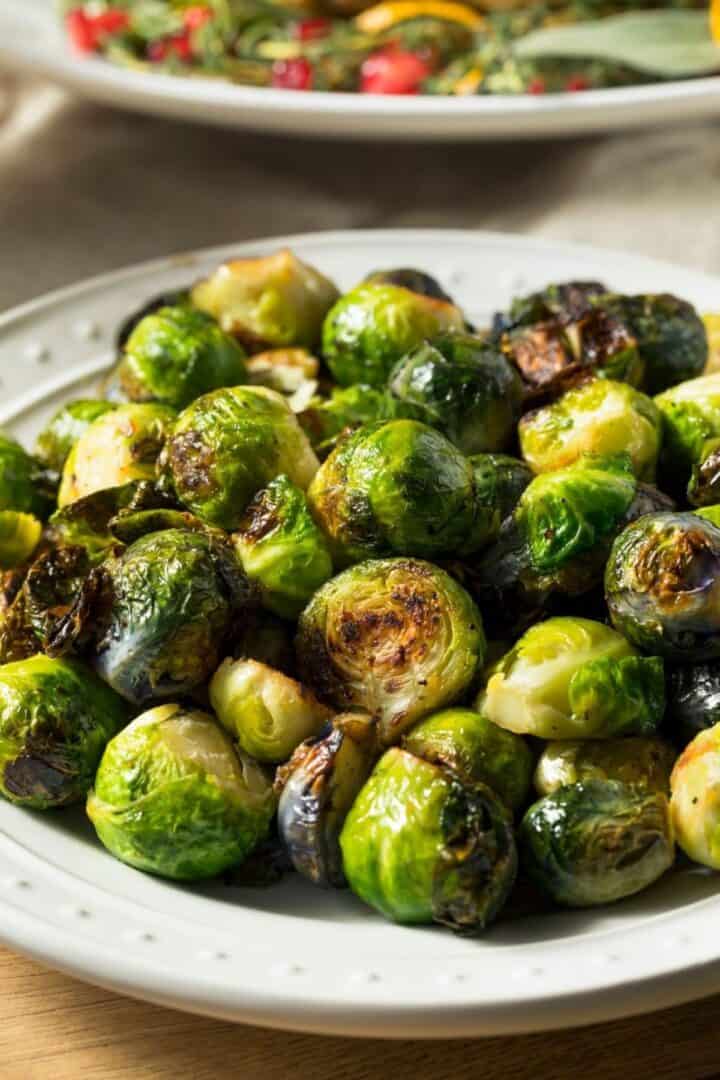 A plate of roasted Brussels sprouts with browned, crispy edges, topped with savory Parmesan cheese, served on a white dish.