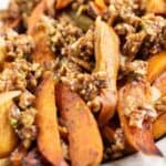 A plate of roasted spicy sweet potatoes wedges topped with a chunky nut and herb mixture.