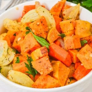 A bowl of Roasted Sweet Potatoes and Carrots, paired with onions, garnished with parsley, and seasoned with herbs.